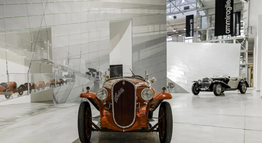 Pomarańczowy Fiat Balilla z 1933 roku na wystawie w Muzeum Fiata w Turynie. W tle inne zabytkowe samochody.