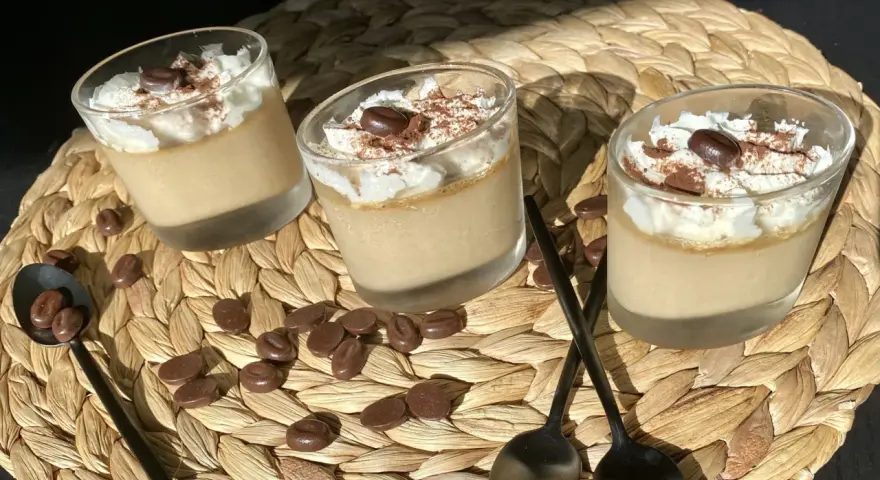 Trois verrines de crème au café facile, garnies de chantilly, cacao et grains de café. Des chocolats en forme de grains parsèment le napperon.
