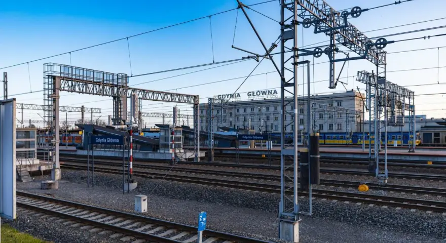 Stacja Gdynia Główna, początek lub koniec najdłuższej trasy kolejowej w Polsce. Tory, perony i budynek dworca pod błękitnym niebem.