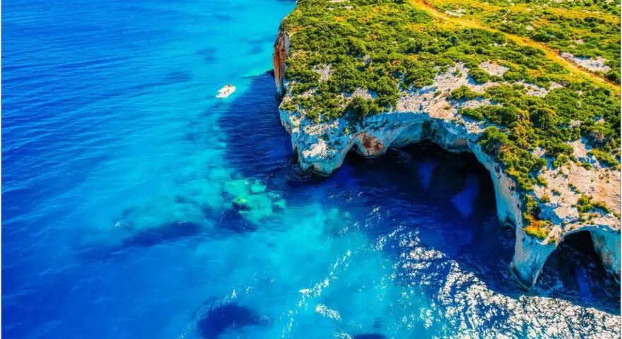 Błękitne morze i klify z jaskiniami to idealne miejsca na Zakynthos, co zobaczyć. Mała łódka kołysze się na falach.