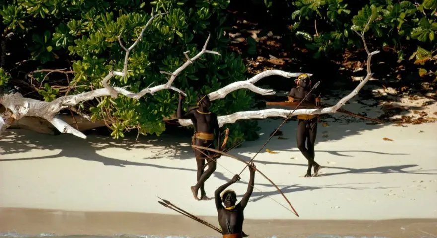 Trzech mężczyzn z plemienia Sentinelese, uzbrojonych w łuki i strzały, stoi na plaży. Sentinel Island, ich dom, chroni ich przed światem.