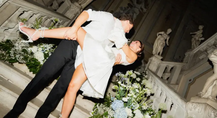 Un couple s'embrasse passionnément sur un escalier orné de fleurs, un moment clé pour réussir son mariage.