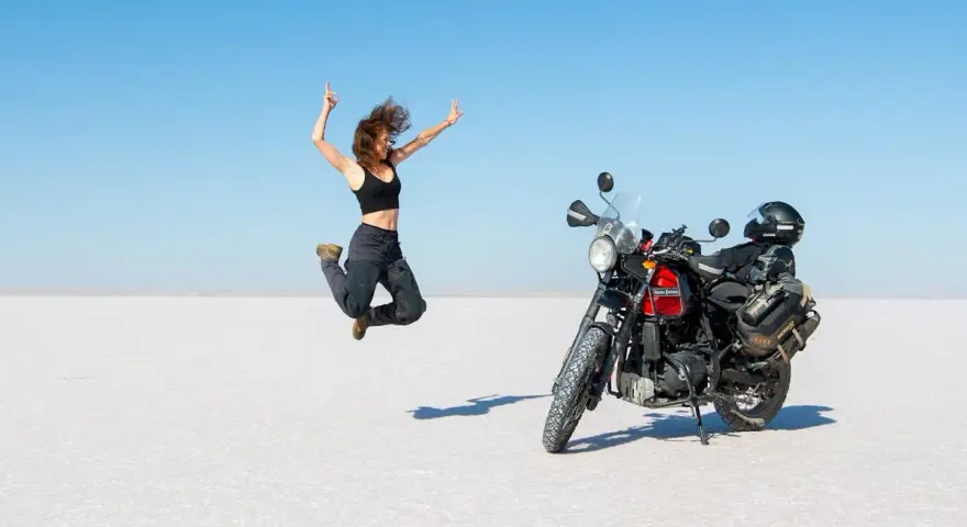 Donna salta di gioia su un deserto di sale, moto pronta per l'avventura. Questo è cosa significa on the road: libertà e scoperta.
