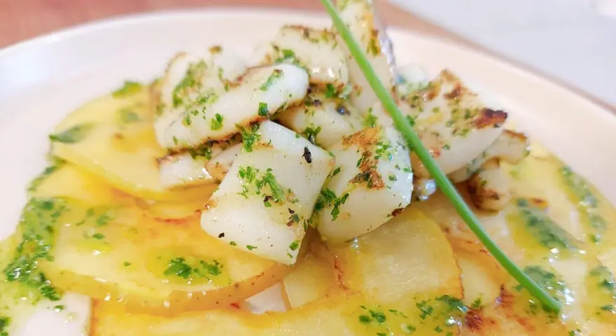 Delicioso plato de sepia al ajillo sobre patatas finas, con perejil picado y un toque de aceite de oliva.