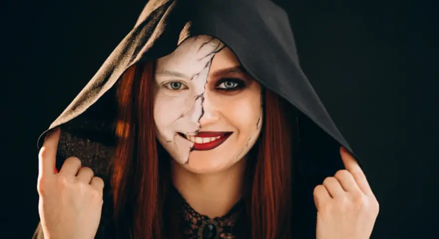 Kobieta w kapturze z połową twarzy pomalowaną na biało, z pęknięciami, druga połowa z ciemnym makijażem. Idealny prosty makijaż na Halloween.