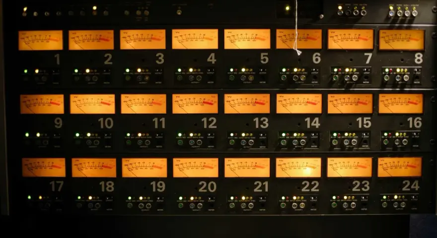 Panneau d'équipement audio avec 24 indicateurs VU orange, chacun affichant un niveau sonore, certains proches de 0 dB, équivalent à 64 décibels.