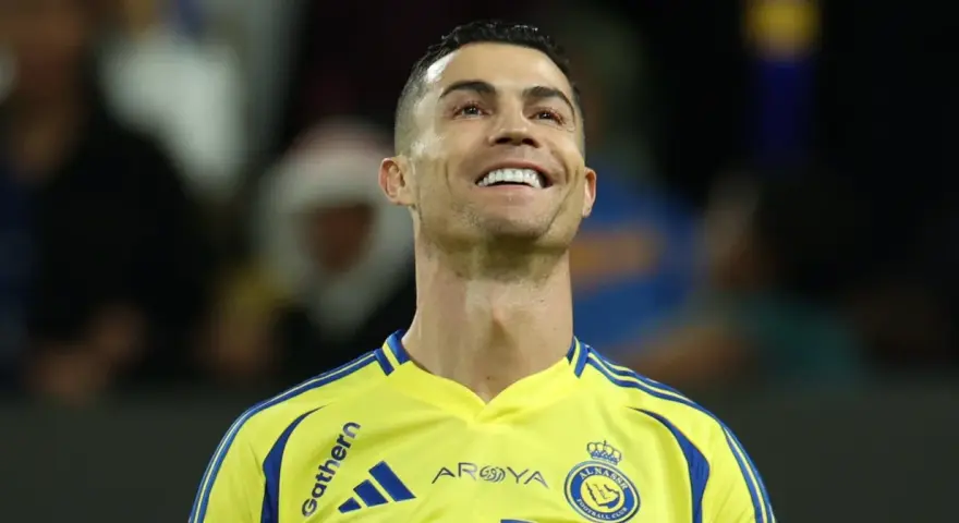 Uśmiechnięty Cristiano Ronaldo w żółtej koszulce Al Nassr. To właśnie w tym klubie gra Ronaldo.