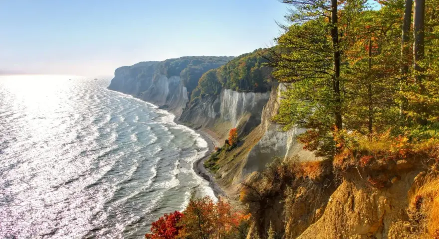Kreidefelsen an der Ostsee, ein malerischer Anblick, der zu den beliebten Urlaubsorten zählt. Das Meer glitzert, Bäume leuchten in Herbstfarben.