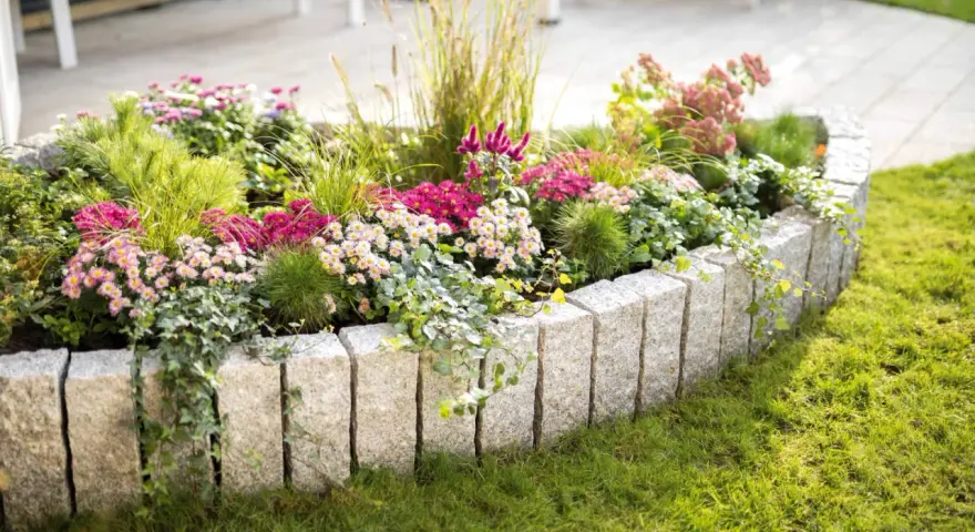 Ein wunderschön bepflanztes Beet mit bunten Blumen und Gräsern, umrandet von Granitsteinen. Perfekt, um neue Ideen für eigene Beet planen zu sammeln.