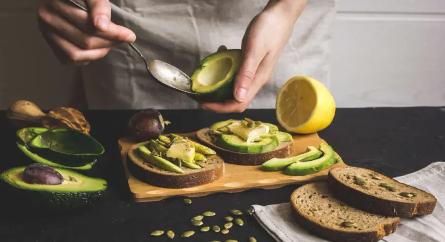 Preparazione di gustose ricette con avocado: toast con avocado, formaggio e semi.