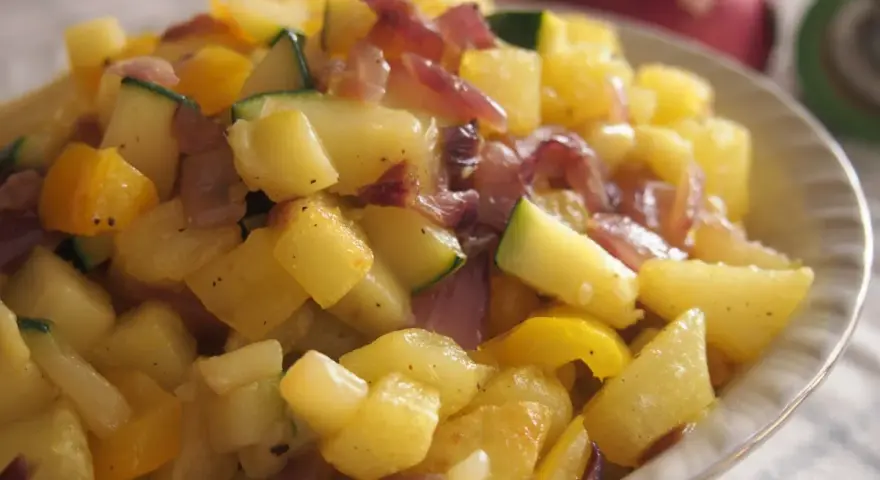 Un delicioso salteado de verduras con patatas, calabacín y pimientos amarillos, con trozos de cebolla morada.