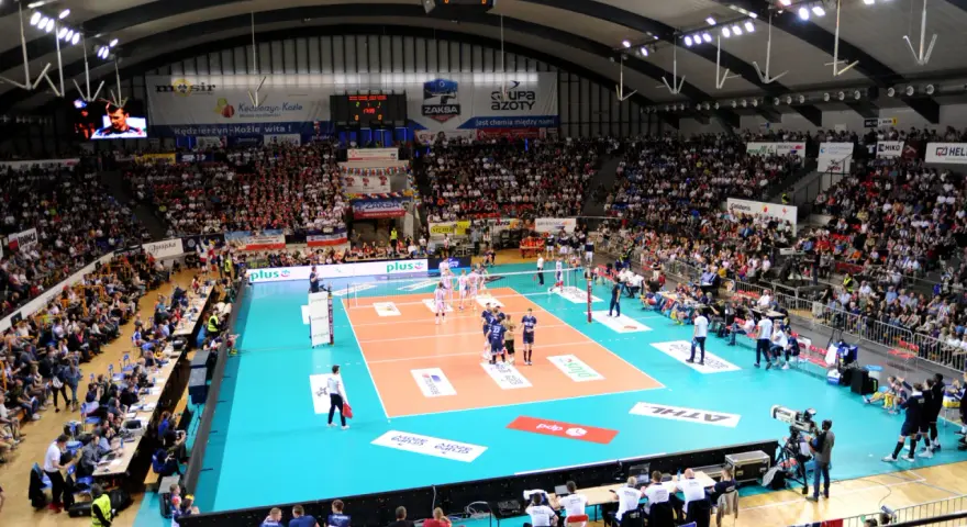 Widownia kibicuje podczas meczu siatkówki ZAKSA. Pełna hala, zawodnicy na boisku, emocje sięgają zenitu.
