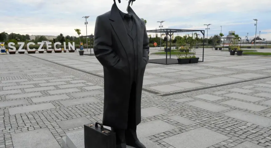 Pomnik Krzysztofa Jarzyny w Szczecinie, z charakterystyczną teczką u stóp, stoi na placu z napisem "SZCZECIN" w tle.