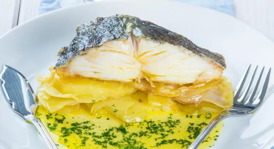 Pescado al horno con patatas y cebolla, bañado en aceite de oliva y perejil. Un plato delicioso y reconfortante.