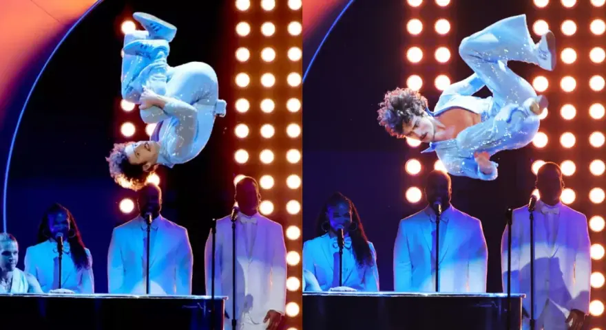 Wokalista w błyszczącym niebieskim stroju wykonuje akrobacje na scenie podczas gali nagród Grammy. Laureaci nagród grammy w białych garniturach stoją za fortepianami.