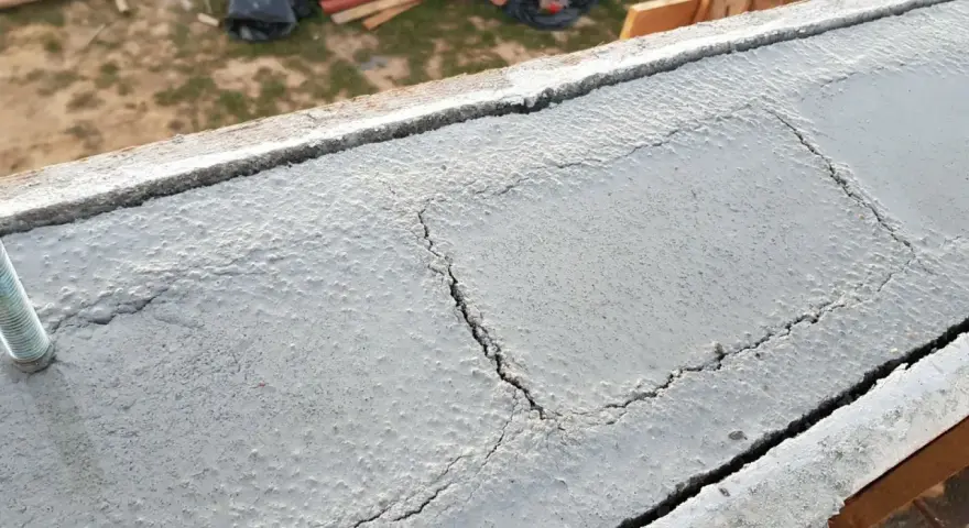 Pęknięty wieniec budowlany z widocznym prętem. Na tle plac budowy.
