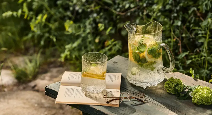 En glasburk med en alkoholfri drink, citron och mynta, står på en bok bredvid ett par glasögon.