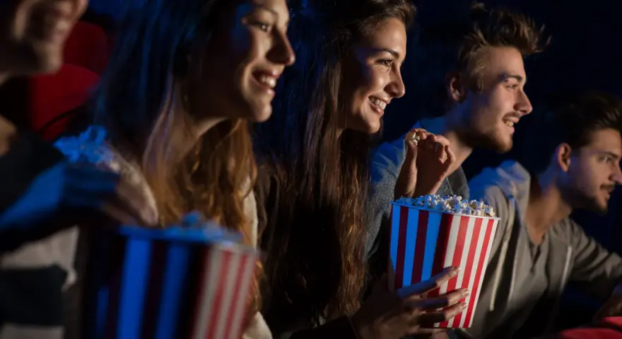Uśmiechnięci ludzie jedzą popcorn w kinie. Idealny strój do kina to coś wygodnego, jak na przykład bluza.