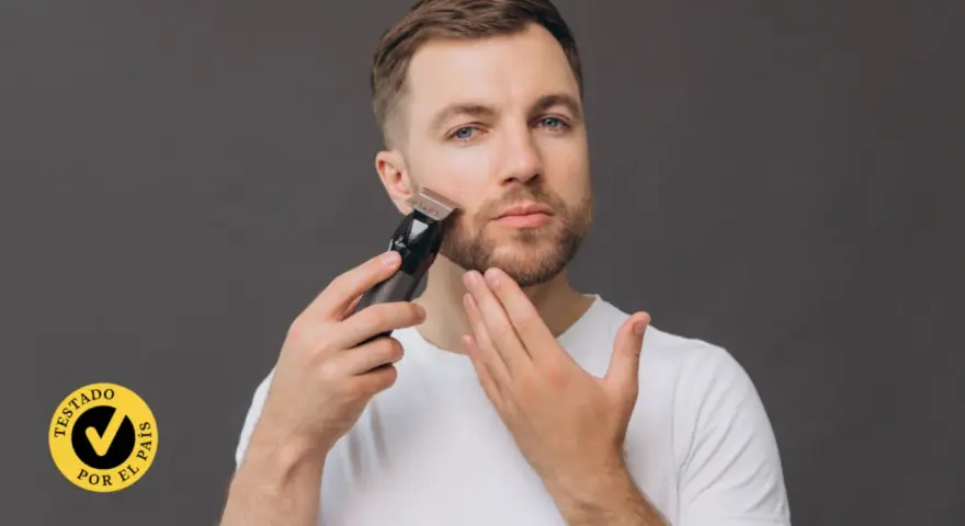 Hombre con barba usando una recortadora para perfilar su rostro. El accesorio "Testado por el país" aparece en la esquina inferior izquierda.