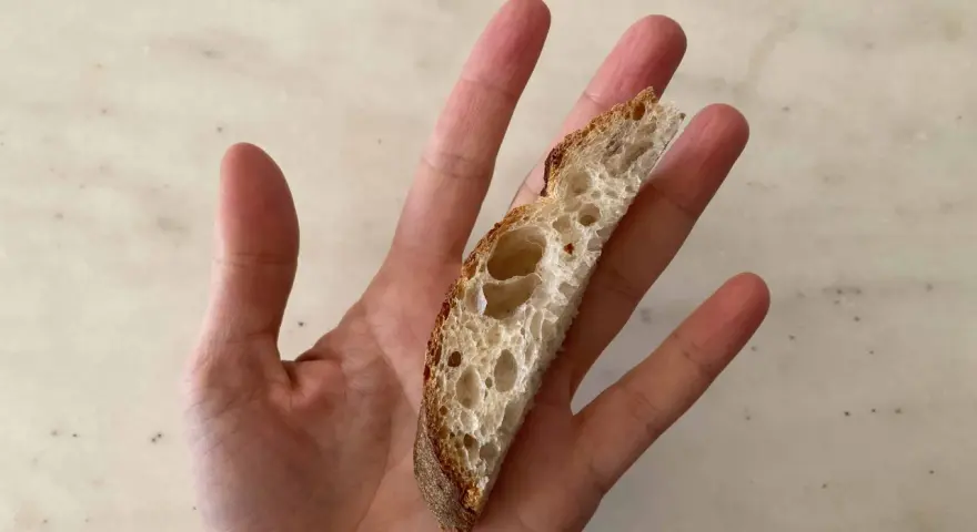 Una mano sostiene una rebanada de pan artesanal, perfecta para el primer pan para bebés.