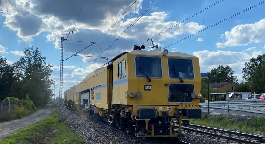 Żółta maszyna torowa DORA jedzie po torach w okolicach Częstochowy. Może to być element rozkładu jazdy prac torowych w Blachowni.