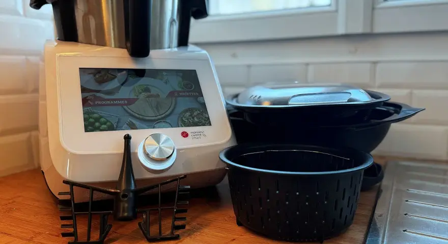 Robot culinaire Monsieur Cuisine Smart prêt à préparer une recette. Accessoires et bols empilés à côté.