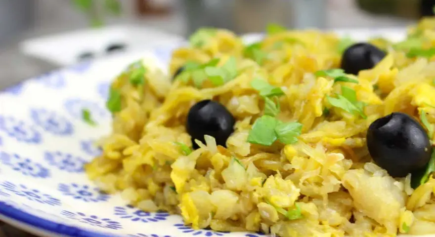 Delicioso bacalao a bras, un plato tradicional con patatas finas, huevo y aceitunas negras, adornado con perejil fresco.