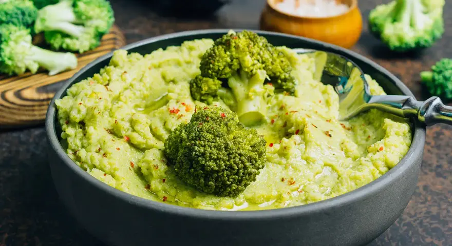 Un bol de purée de brocolis onctueuse, garni de fleurettes de brocolis et d'épices rouges. Un délice vert et sain.