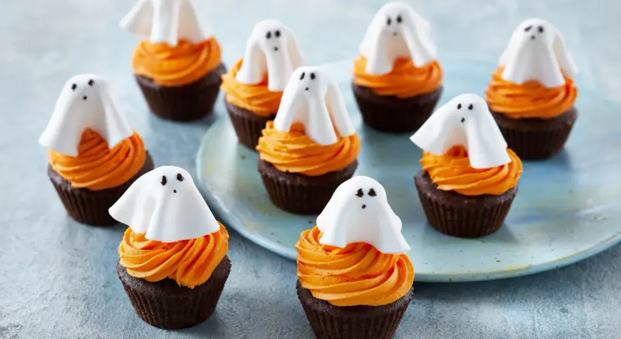 Sju chokladmuffins med orange frosting och vita spökdekorationer. Perfekt att baka till Halloween med barnen!