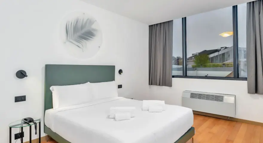A modern hotel room with a king-size bed, white linens, and a green headboard.