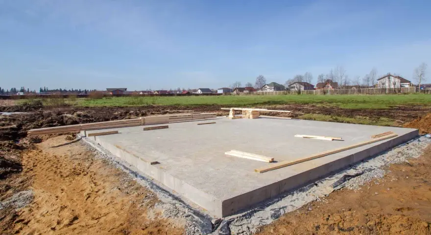 Betonowy fundament domu w budowie. Drewniane deski leżą na płycie. Rozważając budowa fundamentów cena, warto zobaczyć ten etap.