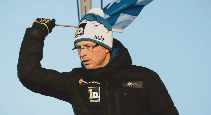 Igor Medved w czapce z pomponem i flagą Finlandii, w czarnej kurtce z logo.