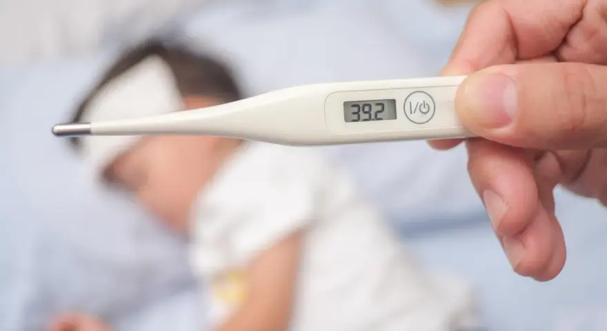 Cyfrowy termometr pokazuje 39.2°C, wskazując wysoką temperaturę ciała u chorego dziecka leżącego w łóżku.