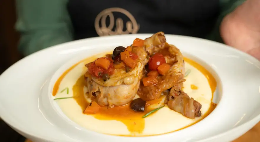 Pollo alla cacciatora succulento su un letto di polenta cremosa, guarnito con pomodorini, olive e carote.