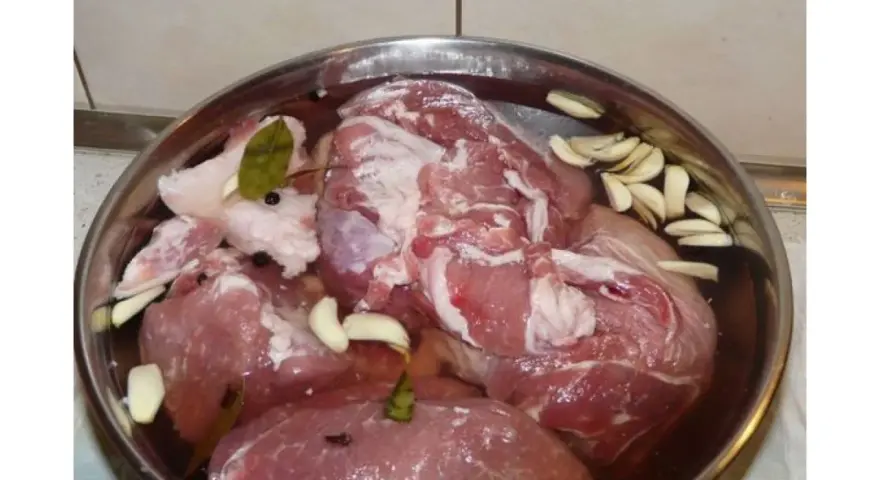 Mięso w misce z wodą, czosnkiem, zielem angielskim i liściem laurowym. To przygotowanie do wędzenia, czyli solanka do wędzenia.