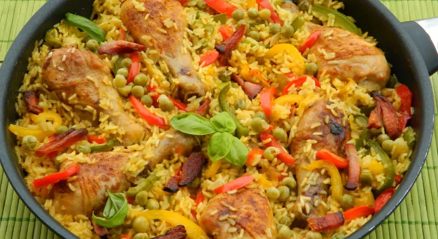 Pyszna paella z kurczakiem, ryżem, papryką i groszkiem w dużej patelni.