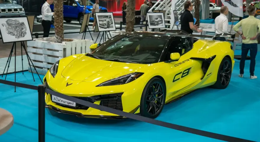 Jaskrawożółty Chevrolet Corvette C8 z czarnym dachem i felgami, prezentowany na niebieskiej podłodze wystawowej.