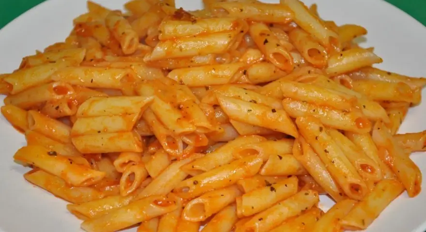 Macarrones penne con salsa de tomate y hierbas en un plato blanco.