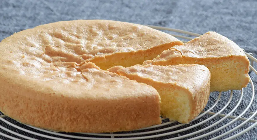 Bizcocho sin gluten esponjoso y dorado, recién cortado en porciones sobre una rejilla.