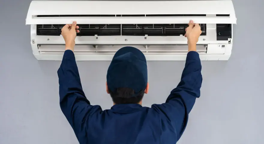 Tecnico con cappellino blu apre il pannello di un climatizzatore per impostare aria fredda.