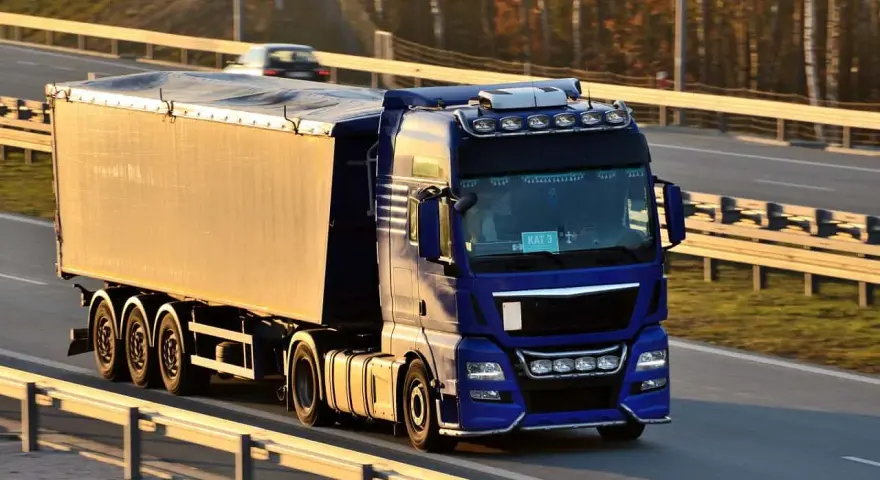 Niebieska ciężarówka z naczepą jedzie autostradą. Kierowca posiada świadectwo kwalifikacji zawodowej, co pozwala mu na bezpieczne przewożenie towarów.