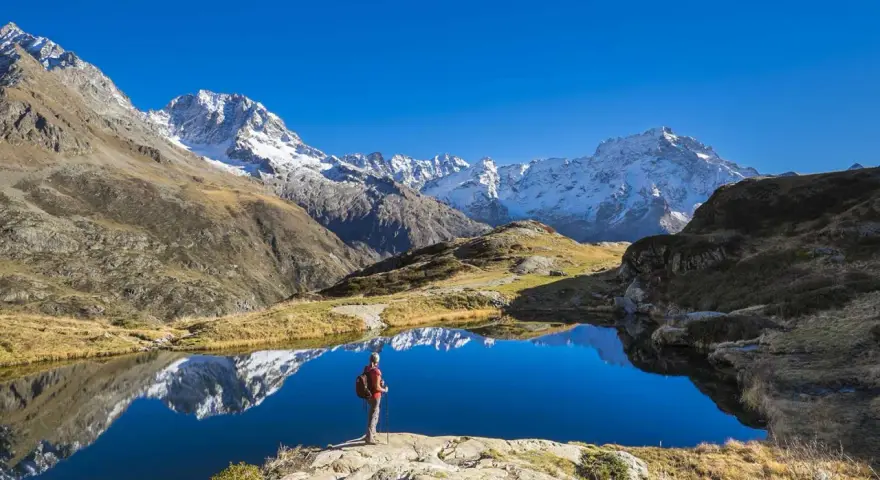 Randonneur contemplant un lac alpin aux reflets parfaits, un paysage grandiose qui pourrait faire partie d'un GR5 itinéraire complet.