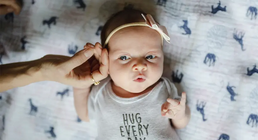 Uroczy 3 tygodniowy noworodek w body z napisem "HUG EVERY DAY", z delikatną opaską na głowie.
