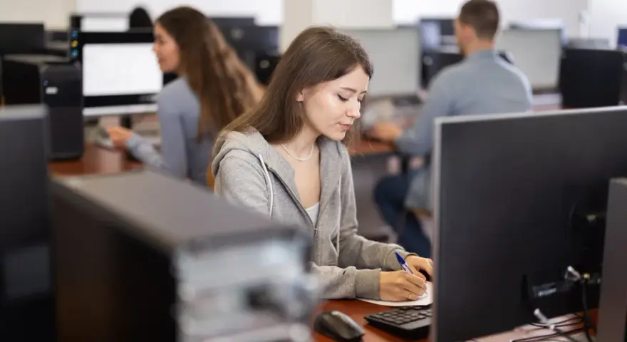 Młoda kobieta, przyszły koder medyczny, skupiona na nauce przy komputerze w sali lekcyjnej.