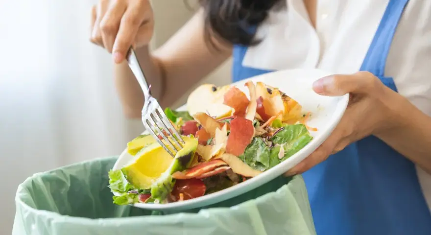 Persona separa restos de comida, como aguacate y cáscaras de manzana, para el reciclaje orgánico.