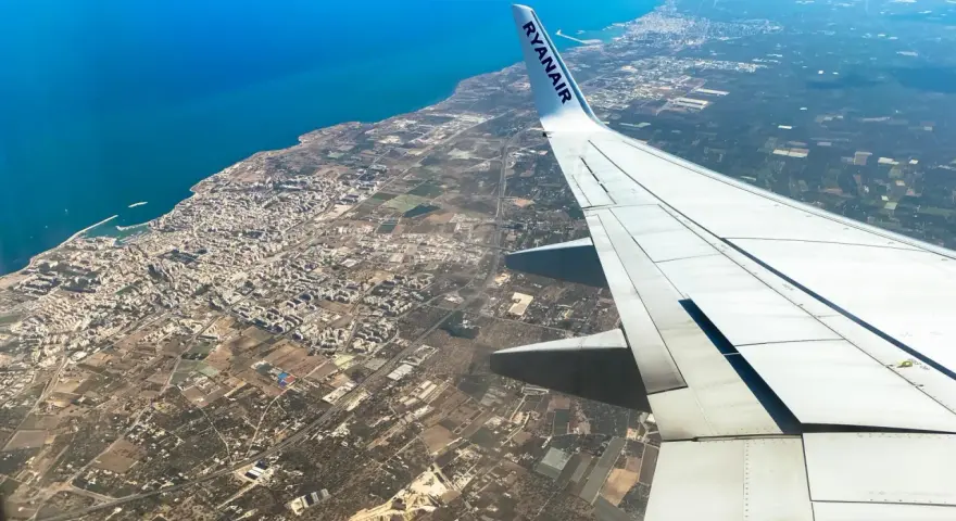 Widok z samolotu Ryanair na wybrzeże i miasto, skrzydło samolotu na pierwszym planie.