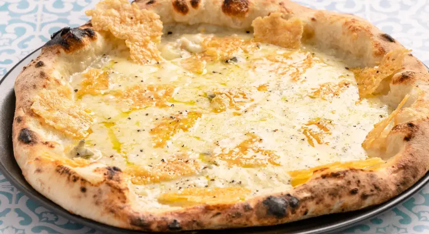 Eine köstliche Pizza quattro formaggi mit geschmolzenem Käse und knusprigem Rand auf einem gemusterten Tisch.