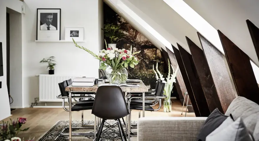 Välkomnande inredd vindsvåning med snedtak, matplats med blommor och konst.