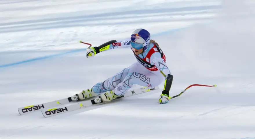 Lindsey Vonn w pełnym pędzie, w białym kombinezonie z napisem USA, na nartach HEAD. Widoczny moment tuż przed upadkiem.