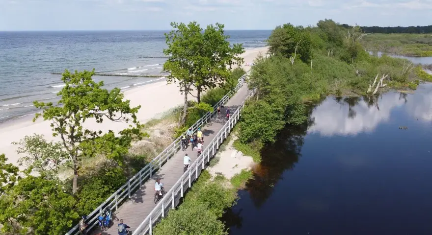 Rowerzyści przemierzają malowniczą trasę EuroVelo 10 wzdłuż plaży i spokojnej wody.